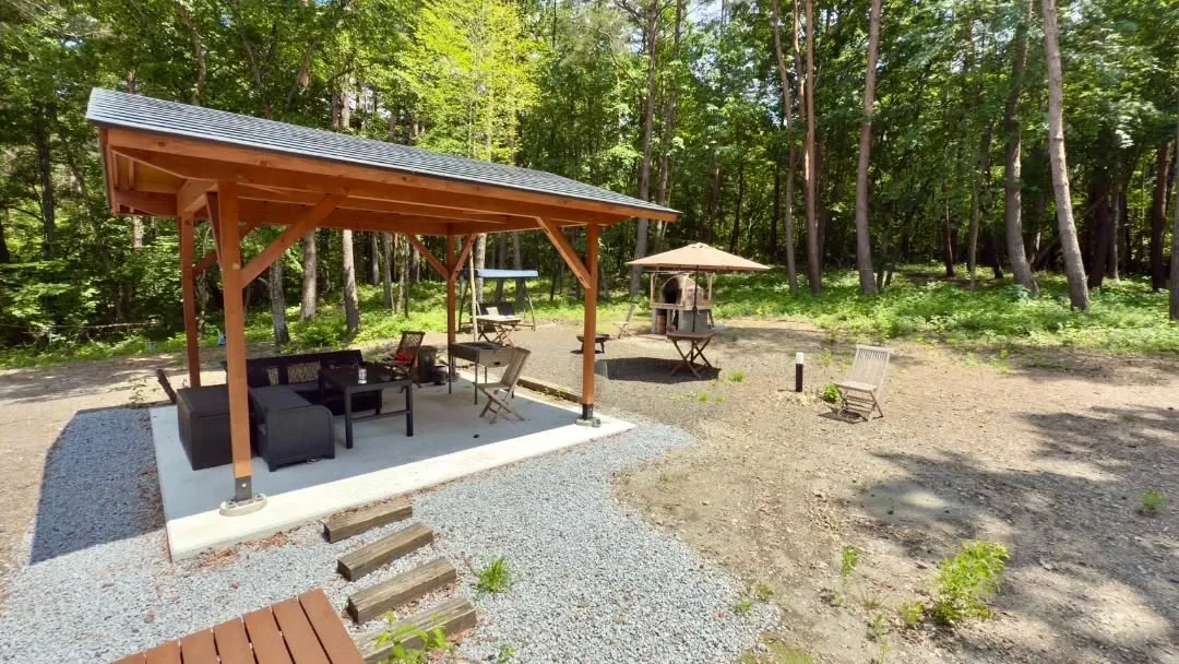 屋根付きのスペースに置かれたテーブルや椅子が、森の中で過ごす...