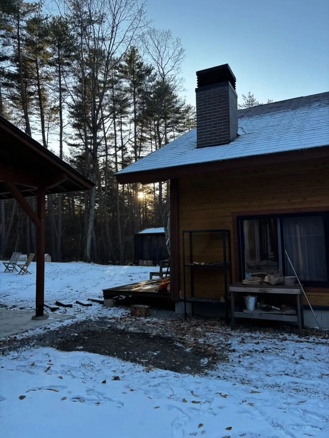 薄く雪が積もった静かな朝、森の奥に佇む建物が淡い光に照らされ...